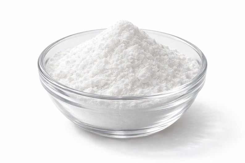 May include: A clear glass bowl filled with a mound of fine white powder. The bowl has a smooth, rounded shape and transparent walls, allowing the texture of the powdery substance to be clearly visible as it rises to a peak in the center.