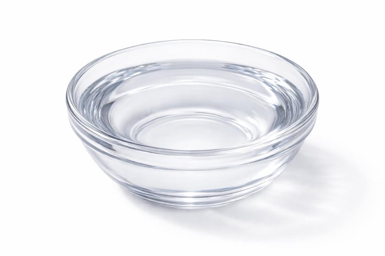 May include: A clear, circular glass bowl with a smooth, transparent surface and a slightly rounded base. The bowl features a simple, open design with a thick rim, showcasing a polished finish that reflects light across its curved structure.