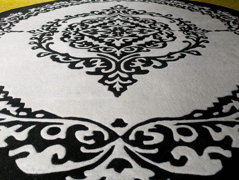 May include: A circular rug featuring a high-contrast black and white color scheme. The design consists of a central black ornate medallion pattern surrounded by a white field, which is enclosed by a wide black border with intricate white scrollwork.