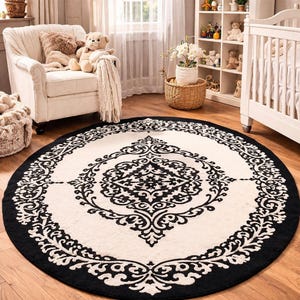 May include: A large circular area rug featuring a cream-colored background with a bold black damask pattern. The design consists of a central ornate medallion surrounded by a wide black border with intricate scrolling floral motifs.