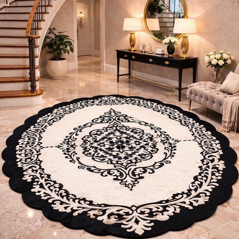 May include: An oval area rug featuring a cream-colored center with a black intricate damask pattern. The rug has a wide black scalloped border with a repeating cream-colored floral motif, creating a high-contrast design on the floor surface.