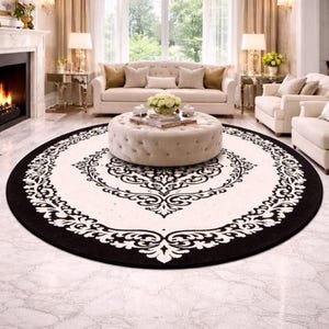 May include: A large circular area rug featuring a cream-colored center and a wide black border. The rug displays a symmetrical black damask-style floral pattern that radiates from the center toward the outer edge, creating a bold contrast.
