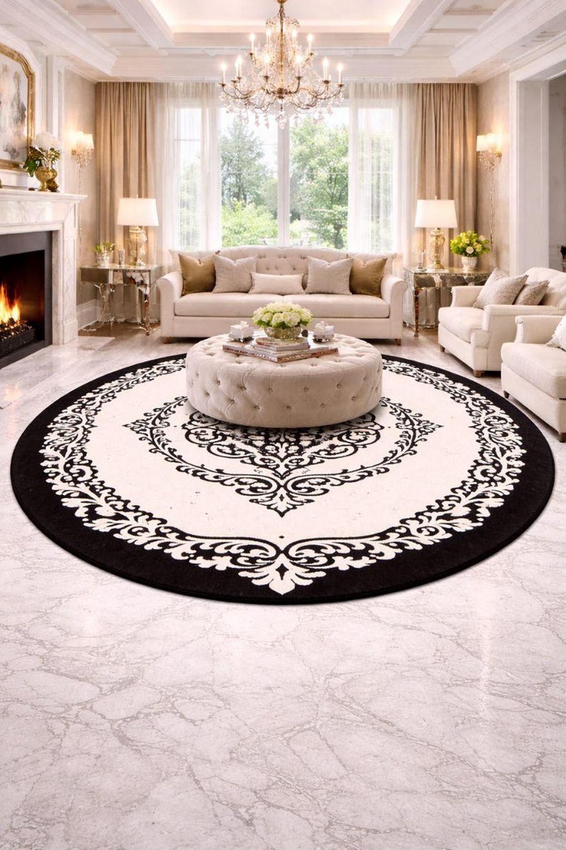 May include: A large circular area rug featuring a cream-colored center and a wide black border. The rug displays a symmetrical black damask-style floral pattern that radiates from the center toward the outer edge, creating a bold contrast.