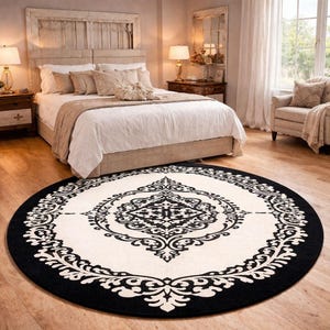May include: A large circular area rug featuring a cream-colored center and a wide black border. The rug displays a symmetrical, intricate black damask-style pattern that radiates from the center toward the outer edge, creating a bold contrast.