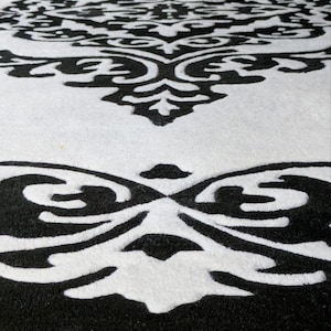 May include: A circular rug featuring a high-contrast black and white damask pattern. The design consists of intricate, symmetrical scrollwork and floral-inspired motifs that repeat across the surface, creating a bold graphic visual effect.