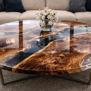 May include: Oval coffee table with a unique design. The tabletop features a glossy, dark brown wood grain pattern with a river of dark blue resin. The table has a metal base and a vase of white flowers.