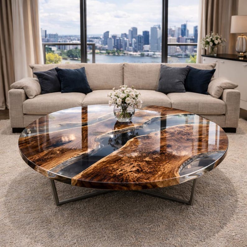 May include: A round coffee table with a unique design. The tabletop features a glossy, dark brown wood grain pattern with a river of dark blue resin. The table has a metal base and sits on a light-colored rug. A beige sofa and city skyline are visible in the background.