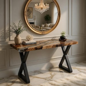 May include: A modern console table with a wood and resin top, supported by black metal legs. A gold-framed mirror hangs above, reflecting a chandelier and living room. Decorative items include a vase, coral, and books.