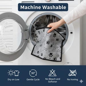 May include: A grey pet mat with black paw prints and bone patterns is being washed in a washing machine. The mat has a black border. The text "Machine Washable" is above the washing machine.