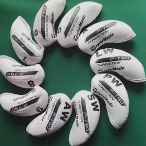 以下が含まれることがあります： 緑色の背景に円を描くように配置された、白いゴルフヘッドカバーのコレクションです。各カバーには、黒で「P.790 TUNGSTEN TaylorMade」と印刷されています。カバーには数字と文字が記載されています。
