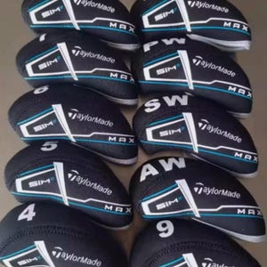 May include: A selection of black golf club head covers, each featuring the TaylorMade logo, SIM, and MAX branding. They have white and teal accent designs. Numbers and letters such as "4", "5", "9", "PW", "SW", and "AW" are printed on the covers.