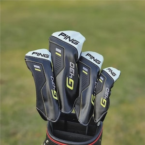 Puede incluir: Un juego de cuatro fundas para palos de golf PING. Las fundas son negras con la parte superior blanca y detalles en amarillo y gris. El texto "PING" y "G430" es visible. Las fundas están en una bolsa de golf negra.