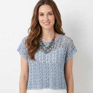 May include: A pale blue crochet top with short sleeves and an open weave design. A multi-strand necklace in blue and grey tones is worn with the top. The model is smiling.