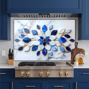 May include: A decorative wall art piece featuring a floral design made of blue and white leaf-shaped elements. The artwork is set against a marble background, with gold accents. The piece is mounted above a stainless steel stove.