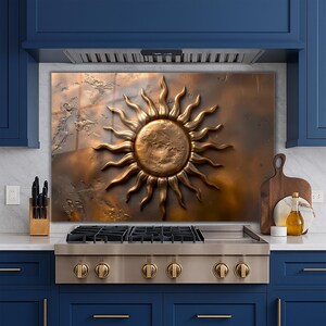 May include: A bronze-colored sunburst wall art with a textured background. The sun has a detailed, three-dimensional design with radiating rays. The artwork is mounted above a stainless steel gas range in a kitchen setting.