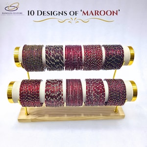 Könnte beinhalten: Präsentation von zehn Designs von maroonfarbenen Armreifen. Die Armreifen sind auf einem zweistufigen Holzständer mit goldenen Akzenten angeordnet. Der Text "10 Designs of 'Maroon'" wird oben im Bild angezeigt.