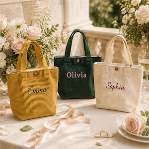 May include: Three small corduroy tote bags with top handles and a single snap button closure. The yellow bag features the name Emma, the dark green bag features the name Olivia, and the cream bag features the name Sophia embroidered on the front.
