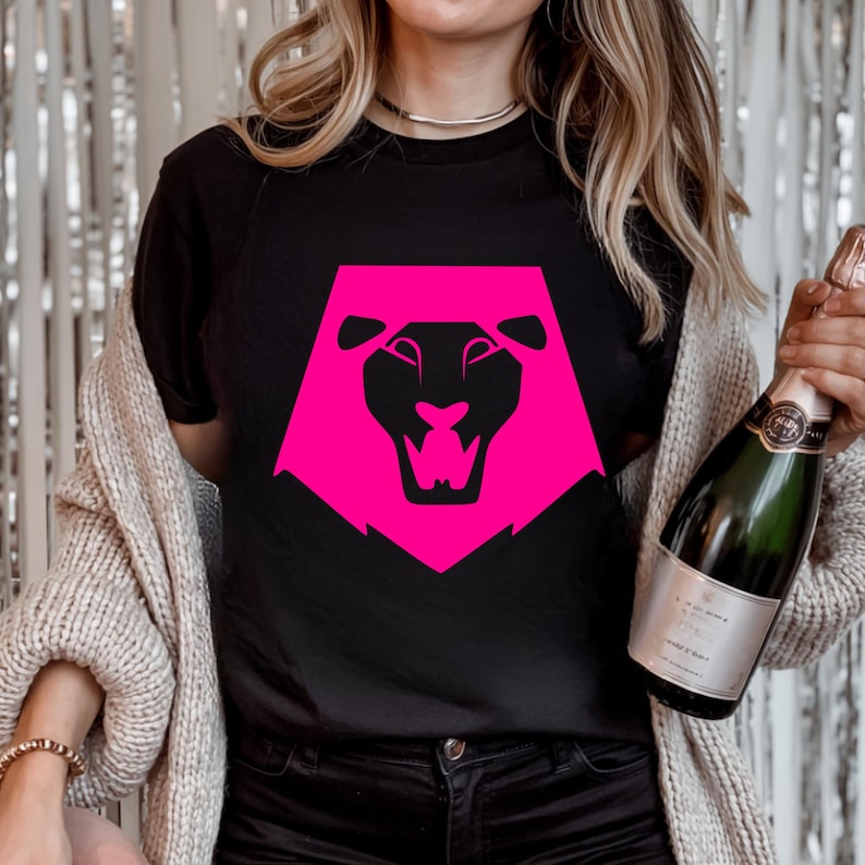 May include: Black t-shirt featuring a vibrant pink lion head design. The lion graphic is a geometric shape with a detailed face and open mouth. The shirt is a classic crew neck style.