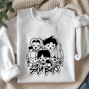 May include: White crewneck sweatshirt featuring a black and white graphic of five cartoon figures. The text "Skit Boys" is below the figures in a stylized font. The sweatshirt is made of a soft material.