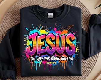May include: Black sweatshirt with the word "JESUS" in a colorful graffiti style. The text is outlined in pink and purple with a brick pattern. Below the word "JESUS" is the text "THE WAY, THE TRUTH, THE LIFE" and "JOHN 14:6".