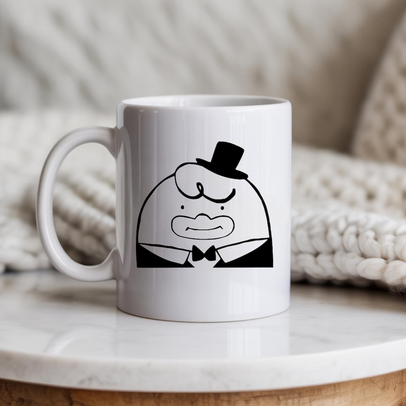 May include: White ceramic mug featuring a cartoon character in a tuxedo and top hat. The black and white illustration depicts a round-faced figure with a bow tie and a stern expression. The mug has a curved handle.