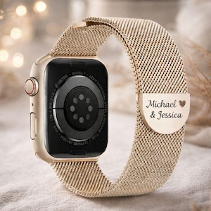 May include: Gold-tone Apple Watch with a mesh band. The watch face is black with white text. The band features the names "Michael & Jessica" and a heart symbol. The watch is a Series 7, 46mm.