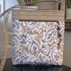 Bolso bandolera o cartera grande de tela acolchada con bolsillo frontal con cremallera, ribete superior y bolsillo trasero con estampado Ikat en gris, azul y beige