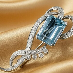 Puede incluir: Broche plateado con una gran gema rectangular de color azul claro en el centro. El broche está adornado con numerosas gemas pequeñas y transparentes y tiene un diseño curvo y fluido. El fondo es una tela de color amarillo dorado.