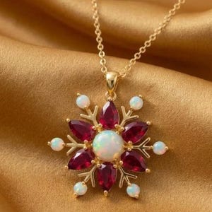 May include: A gold-toned necklace featuring a snowflake-shaped pendant. The center is a round iridescent opal, surrounded by six pear-shaped deep red gemstones and six smaller round white opals set at the tips of the metal snowflake branches.