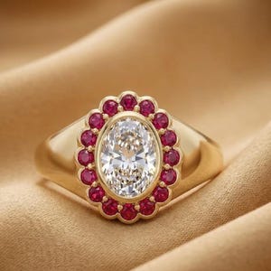 May include: A gold ring featuring a large, central oval-cut white gemstone surrounded by a scalloped halo of small, round, vibrant red rubies. The band is smooth and polished, showcasing a classic design with a prominent, multi-stone setting.