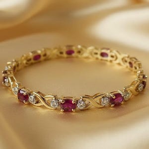May include: A gold bracelet with alternating oval-cut red gemstones and small round white gemstones. The bracelet has a delicate, interwoven design and is set against a soft, golden background.