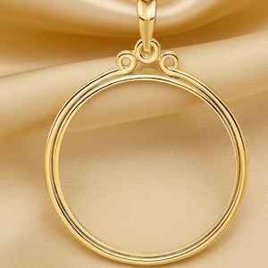 May include: A gold pendant featuring a circular frame and decorative top detailing. The pendant has a heart-shaped bail and ornate swirls above the circular frame. The background is a soft, golden fabric, creating a luxurious feel.
