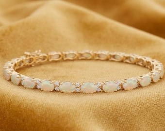 Op de afbeelding: Een gouden tennisarmband met een reeks ovaalvormige opalen afgewisseld met kleine, heldere ronde stenen. De armband is geconstrueerd met individuele metalen schakels die elke edelsteen verbinden, wat een flexibele, cirkelvormige ketting vormt.