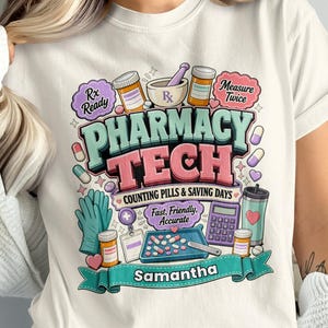 May include: A cream-colored t-shirt featuring a colorful graphic with the text PHARMACY TECH, COUNTING PILLS & SAVING DAYS, Fast, Friendly, Accurate, Rx Ready, Measure Twice, and Samantha. The design includes pill bottles, a mortar and pestle, a calculator, a pill tray, gloves, and various capsules.