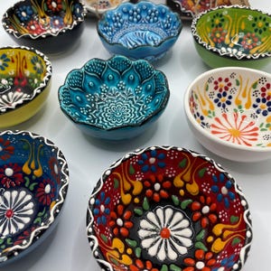 May include: A collection of small, decorative ceramic bowls with intricate floral patterns in various colors. The bowls feature a scalloped edge and a glossy finish. Colors include blue, green, red, yellow, and white. These bowls are likely for serving small portions or as decorative items.