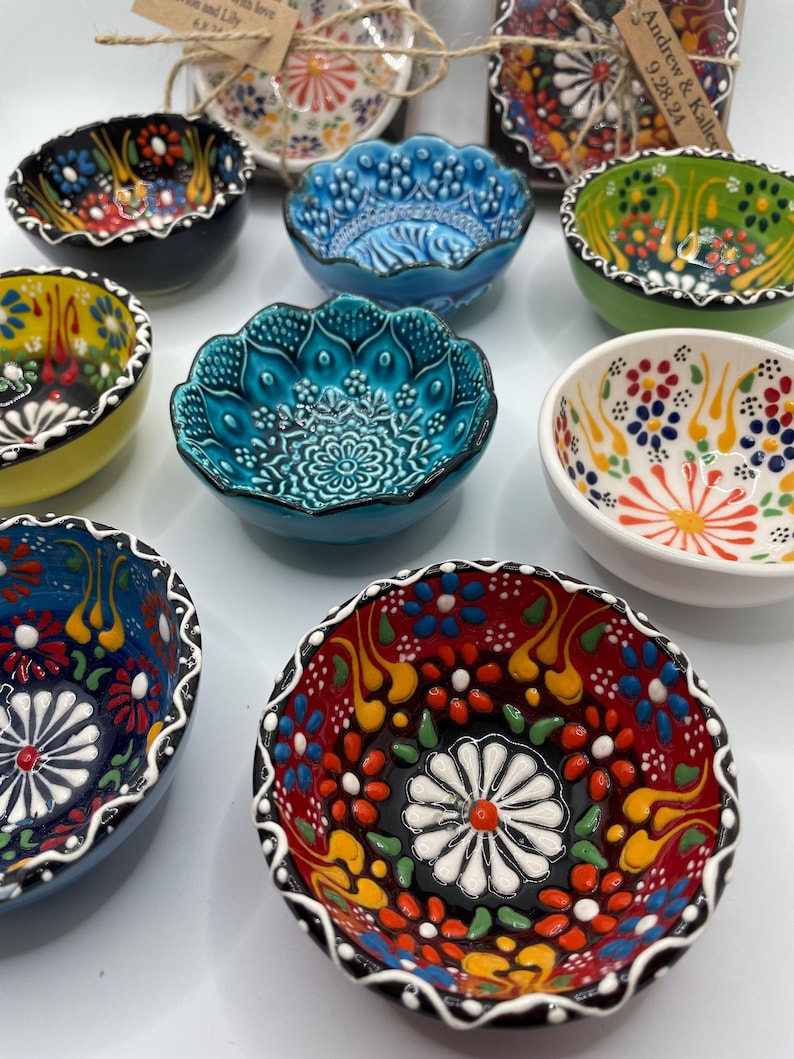 May include: A collection of small, decorative ceramic bowls with intricate floral patterns in various colors. The bowls feature a scalloped edge and a glossy finish. Colors include blue, green, red, yellow, and white. These bowls are likely for serving small portions or as decorative items.