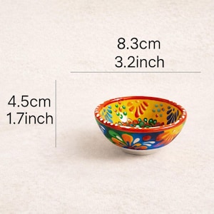 May include: A small, hand-painted ceramic bowl with a vibrant floral design. The bowl is 3.2 inches in diameter and 1.7 inches tall. The rim is red, and the interior features yellow, blue, and orange colors.