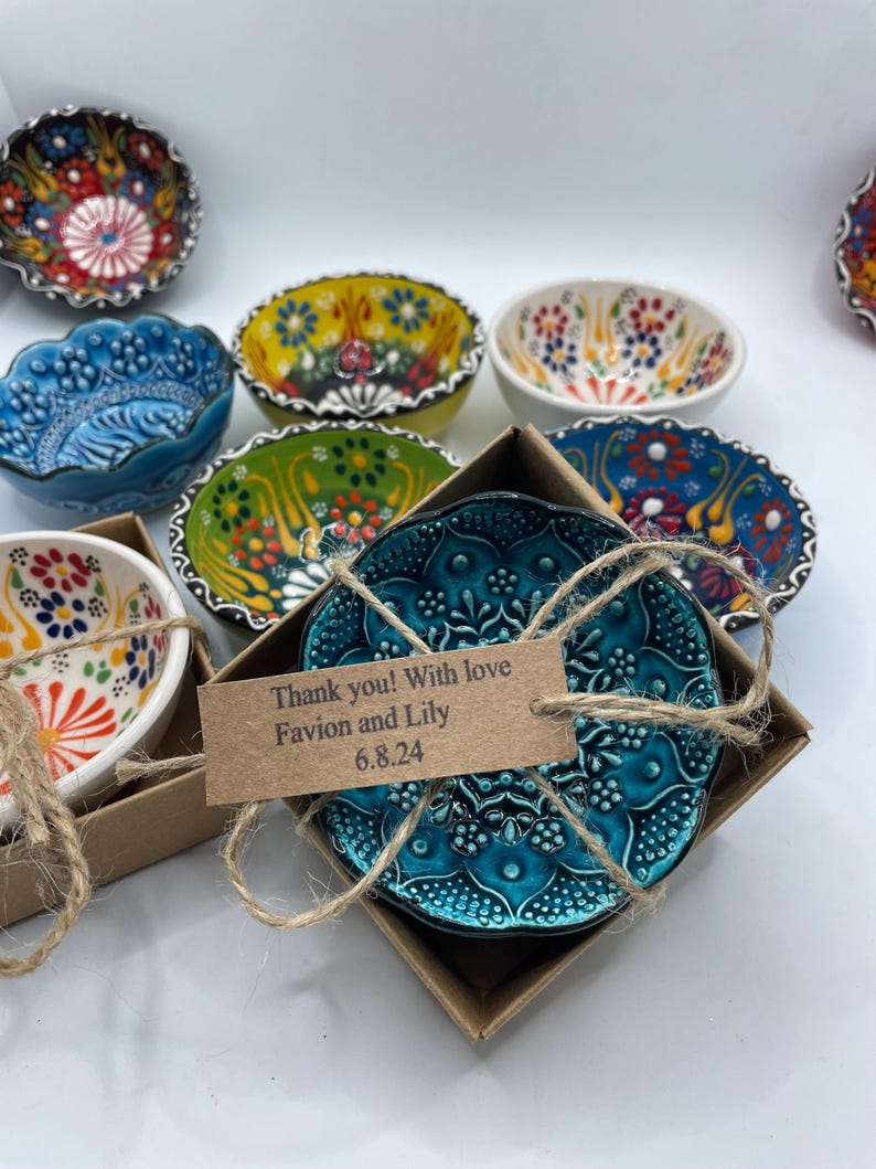 May include: A collection of small, decorative ceramic bowls with intricate floral patterns in various colors. One teal bowl is in a box with a tag that reads "Thank you! With love Favion and Lily 6.8.24". The bowls are ideal for serving small portions.