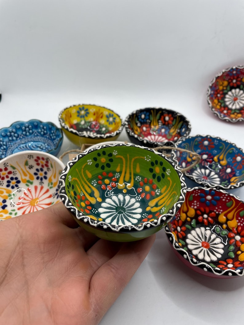 May include: A collection of small, hand-painted ceramic bowls with intricate floral designs. The bowls feature a variety of colors, including green, yellow, blue, and red, with white and black accents. The bowls are likely for serving dips or small portions.
