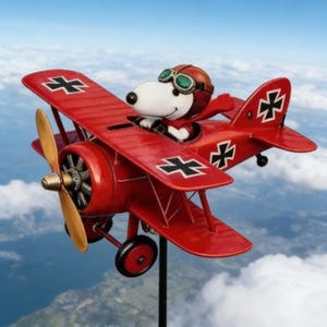 May include: A red biplane with a cartoon character in the cockpit, wearing a brown aviator helmet and goggles. The plane has a wooden propeller and black and white cross symbols on the wings and tail. The background is a blue sky with clouds.