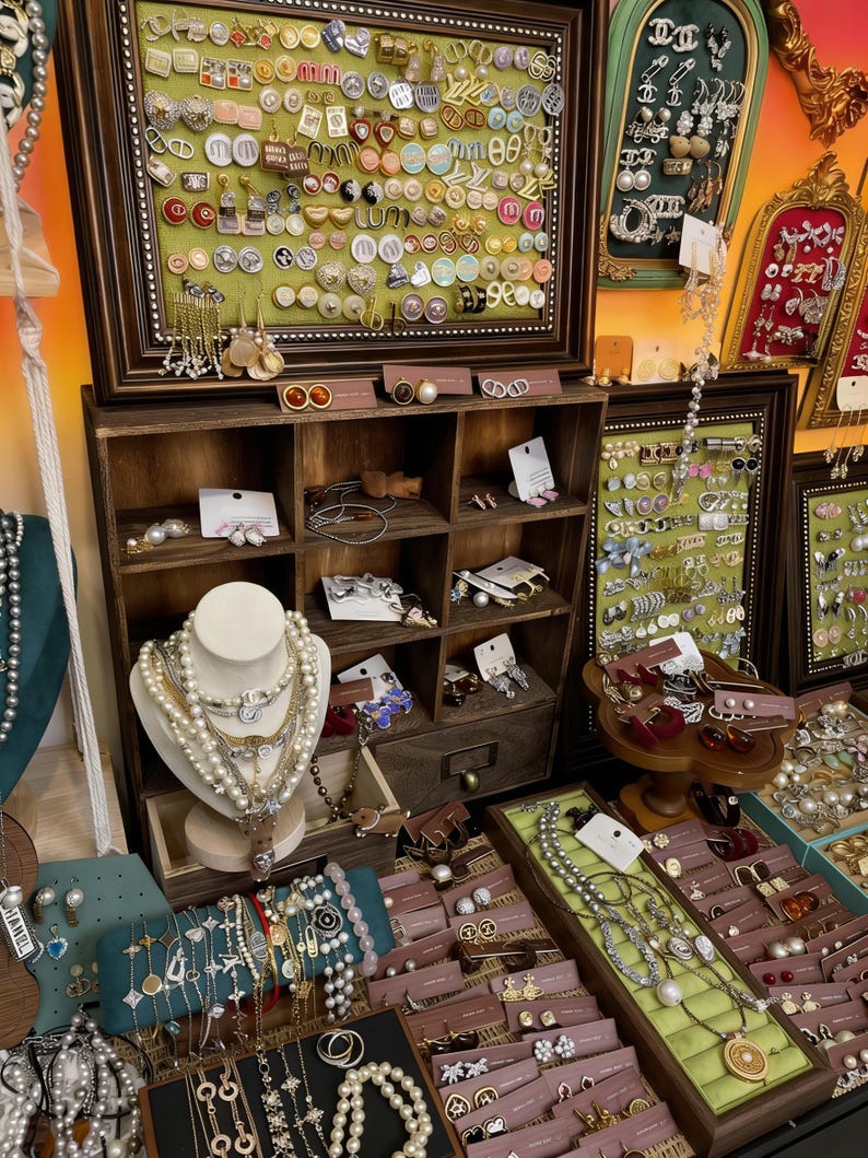 May include: A shop display showcasing a variety of jewellery pieces. Necklaces, earrings, and bracelets are arranged on wooden shelves and display cases. The jewellery features pearls, gold, and silver, in diverse styles and colours.