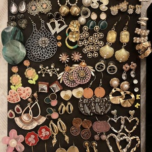 May include: A selection of earrings on a black background. The earrings showcase a variety of designs, such as floral, geometric, and abstract forms. Materials include metal, pearls, and colourful accents. Styles vary from studs to drop earrings.