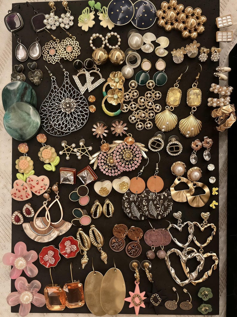 May include: A selection of earrings on a black background. The earrings showcase a variety of designs, such as floral, geometric, and abstract forms. Materials include metal, pearls, and colourful accents. Styles vary from studs to drop earrings.