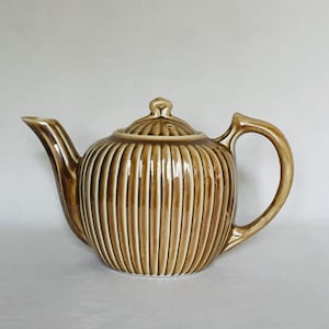 May include: A brown ceramic teapot with vertical lines and a lid. The teapot has a rounded body and a handle.