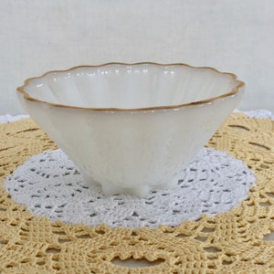 May include: White milk glass bowl with a gold rim and three small feet. The bowl is sitting on a white and yellow crocheted doily.