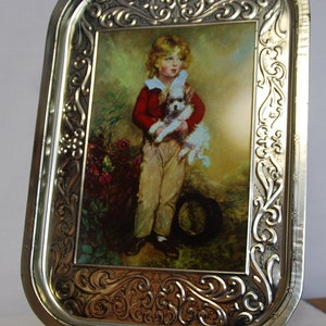 May include: Silver-toned metal serving tray with a decorative embossed border. The tray features a painted image of a child holding a small dog. The child is wearing a red jacket and tan pants. The background has a garden scene.