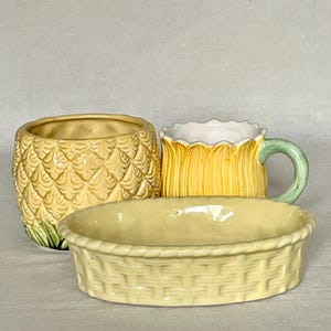 May include: A ceramic pineapple-shaped bowl with a textured yellow exterior, a yellow mug with a scalloped rim and a green handle, and an oval-shaped yellow ceramic dish featuring a woven basket-weave pattern on its exterior surface.