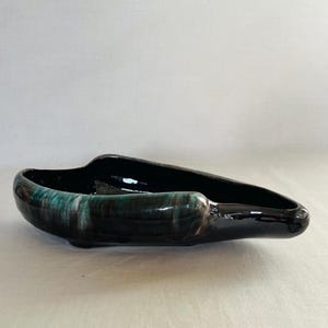 May include: A black and green ceramic planter with a unique, asymmetrical shape. The planter has a glossy finish and a subtle swirl pattern.
