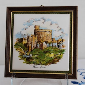 May include: A framed tile with a colorful illustration of Windsor Castle, a large, historic castle with a tall tower. The tile is surrounded by a green and gold frame.