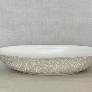 May include: A large, oval-shaped ceramic bowl with a textured, speckled exterior in shades of beige and white. The interior is smooth and white. This decorative bowl is suitable for serving or display.